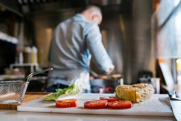 Sandwich and tomato slices on cutting board while chef cooking food in background at restaurant model released Symbolfoto property released EGAF02311