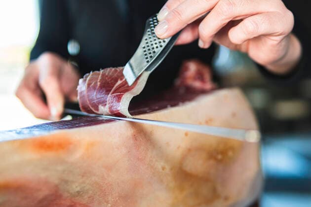 Young female chef cutting slice of ham with kitchen knife model released Symbolfoto property released JAQF00533