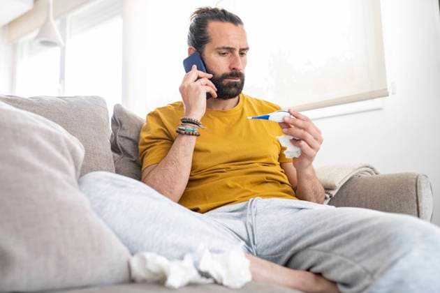 Worried man talking on smart phone while looking at thermometer at home model released Symbolfoto property released JCCMF01941