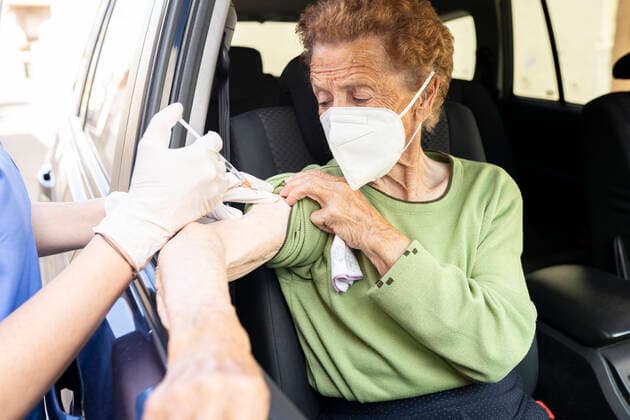 Female doctor vaccinating senior woman in car model released Symbolfoto JCCMF01983