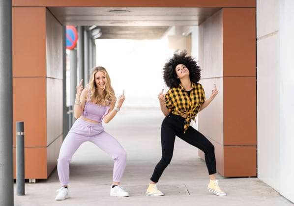 Female friends making obscence gesture while dancing at parking lot model released Symbolfoto JCCMF02353
