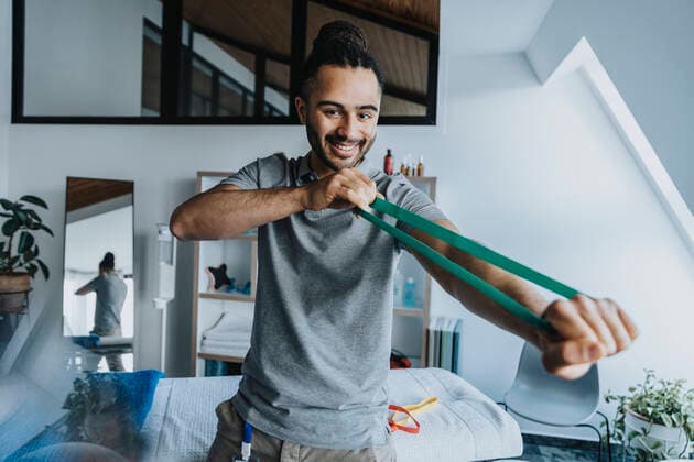 Smiling male physical therapist stretching resistance band in practice model released Symbolfoto property released MFF07729