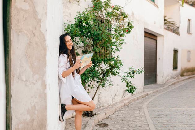 IMAGO Creative: Welttourismustag am 27. September Smiling woman checking map while standing on footpath model released Symbolfoto MRRF01059