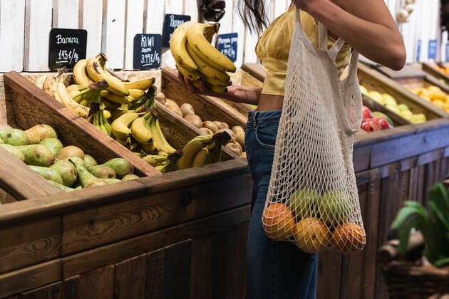 Young woman with mesh bag buying bananas at grocery store model released Symbolfoto property released PNAF01567