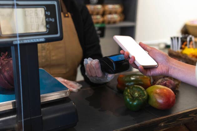 IMAGO Creative: Business, Inflation und Lieferketten Woman holding smart phone over credit card reader while paying at grocery store model released Symbolfoto property released PNAF01593