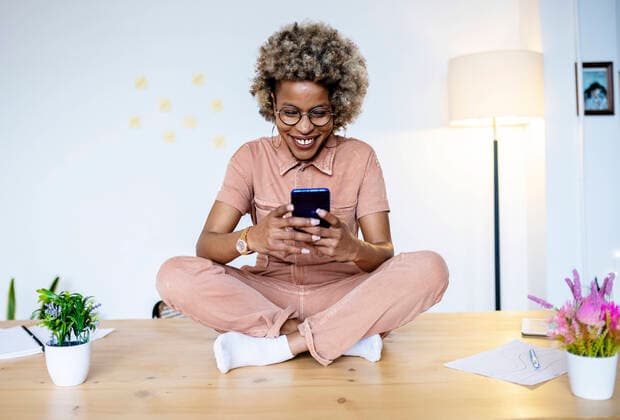 Female professional using smart phone while sitting cross-legged on desk at home office model released Symbolfoto property released RFTF00067
