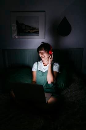 IMAGO Creative, Weihnachten, Tradition: Weihnachtsfilme sehen Smiling woman wearing headphones using laptop at darkroom model released Symbolfoto property released TCEF01772