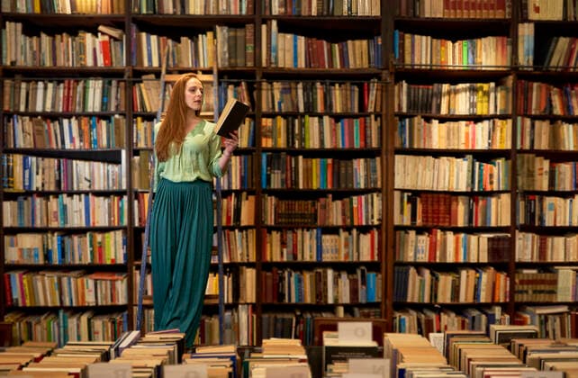 Dedicated woman reading book while standing on ladder in library model released Symbolfoto property released VEGF04387