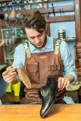 IMAGO Creative: Kreative Renaissance -- der junge Entrepreneur Male entrepreneur holding shoe stretcher while looking at shoe at workshop model released Symbolfoto property released VGF00360