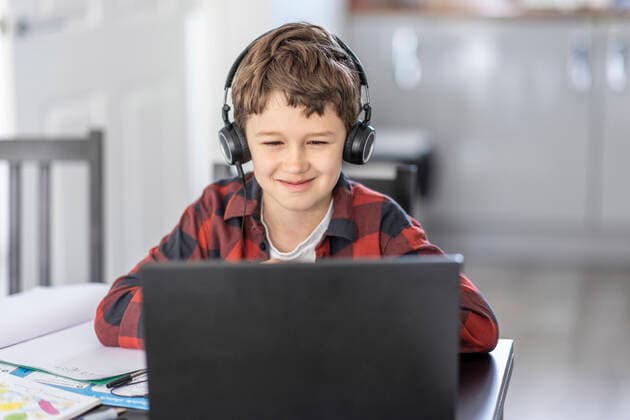 Smiling boy attending online classes through laptop while e-learning at home model released Symbolfoto property released WPEF04371