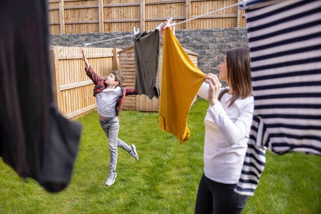 Mother looking at boy touching clothesline while jumping on grass in back yard model released Symbolfoto property released WPEF04385