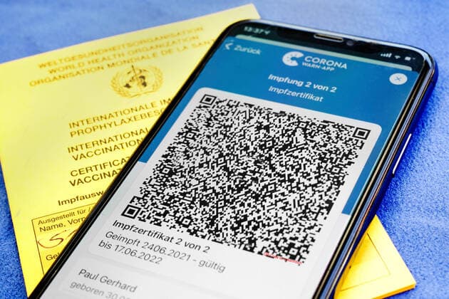QR-Code, das digitale Impfzertifikat in der Corona Warn-App auf einem Smartphone bestätigt eine abgeschlossenen Impfung gegen Covid-19. Liegt auf der gelben Internationalen Impfbescheinigung, Impfpass. - ACHTUNG! QR-Code und persönliche Angaben sind unkenntlich gemacht!