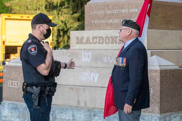 Kanada, Entfernung der Statue von ex-Premierminister John Macdonald in Kingston, Ontario June 18, 2021, Kingston, Ontario, Canada: A Kingston Police officer talks with a man holding a Canadian flag before the removal of the statue of Sir John A. Macdonald in Kingston, Ontario on Friday June 18, 2021. The statue will be removed from a park in his hometown of Kingston while his name will be taken off a local school. Kingston s city council voted this week to take the statue from City Park, place it temporarily in storage, and eventually put it up in Kingston Cataraqui Cemetery where Canada s first prime minister is buried. Kingston Canada - ZUMAc35_ 20210618_zaf_c35_007 Copyright: xLarsxHagbergx