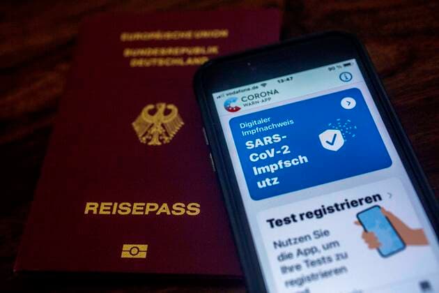 Bescheinigung über eine erfolgte, doppelte Corona-Schutzimpfung im Impfausweis und in der Coronawarnapp auf einem iPhone und ein Reisepass. Reisepass - Impfpass