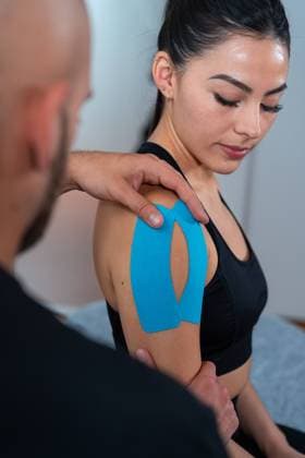Bearded male physiotherapist applying kinesio tapes on shoulder of female athlete during rehabilitation process in hospital, Model released Copyright: xEnriquexEspinosax MR