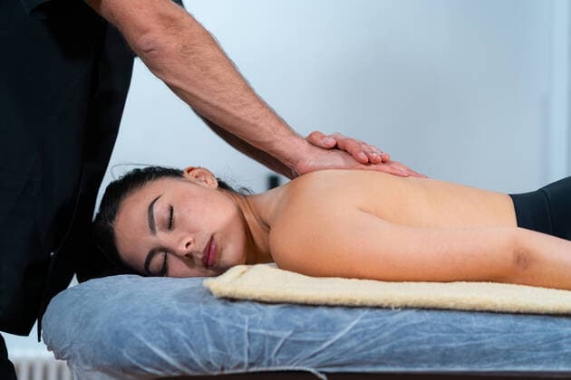 Anonymous physical therapist in black uniform massaging back of topless woman on table against shelves in hospital, Model released Copyright: xEnriquexEspinosax MR
