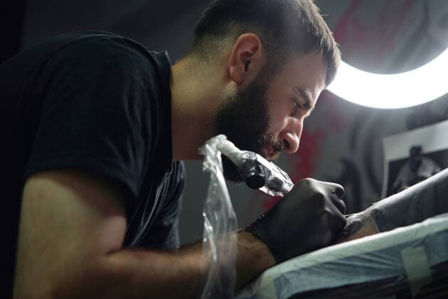 IMAGO Creative: Kreative Renaissance -- der junge Entrepreneur Concentrated male tattooist in gloves making tattoo on hand of client while using professional tattoo machine in modern tattoo studio, Model released, Property released Copyright: xSergeyxMironovx MR