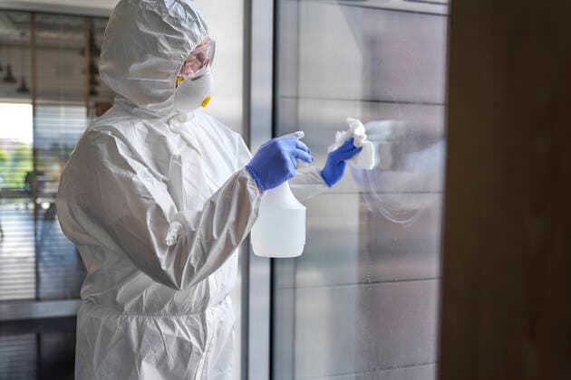 Female sanitation worker spraying chemical on glass while disinfecting office building model released Symbolfoto property released ABIF01368