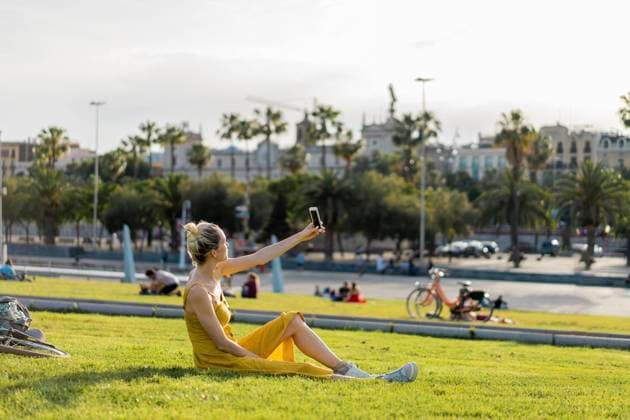 IMAGO Creative: Sommer, Sommertage im Stadtpark Young woman taking selfie through smart phone while sitting at park model released Symbolfoto AFVF08865