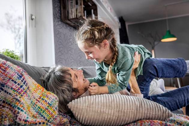 IMAGO Creative: Hygge - Winter Innendesign Grandmother playing with granddaughter while lying on sofa at home model released Symbolfoto property released AUF00617