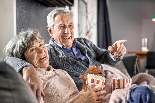 IMAGO Creative: Jahreszeit Winter, Couching Senior couple sitting with popcorn on sofa at home model released Symbolfoto property released AUF00625