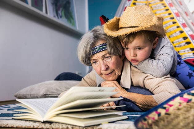 Senior woman reading book while boy lying on her at home model released Symbolfoto property released AUF00662