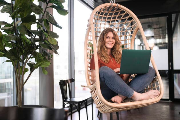 Smiling businesswoman with laptop sitting on swing chair at office cafeteria model released Symbolfoto property released FKF04337