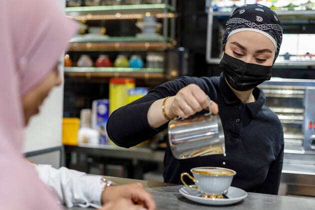 Waitress wearing bandana pouring milk in cup at coffee shop model released Symbolfoto property released IFRF00659
