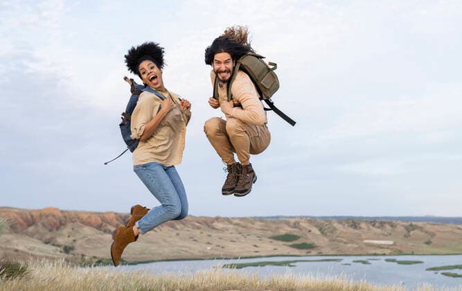 Carefree couple with backpacks jumping together model released Symbolfoto JCCMF02816
