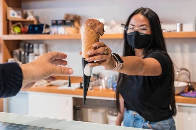 Female employee giving ice cream to customer at store during COVID-19 model released Symbolfoto property released JRVF00873