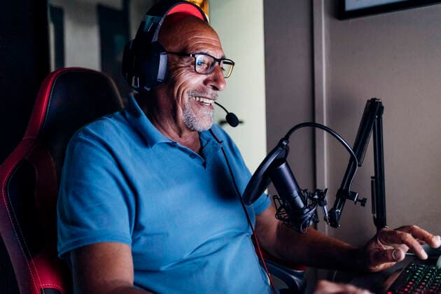IMAGO Creative, Lifestyle, Gaming Smiling senior man wearing headphones using keyboard while playing video game at home model released Symbolfoto property released MEUF03131