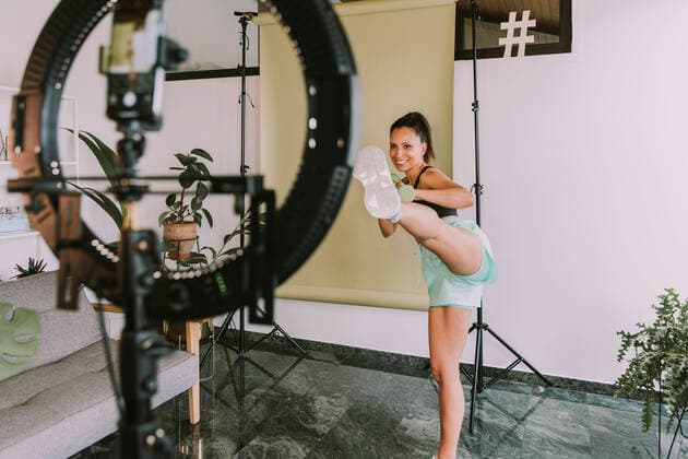 Female fitness trainer showing kicks near backdrop while vlogging at home model released Symbolfoto property released MFF08095