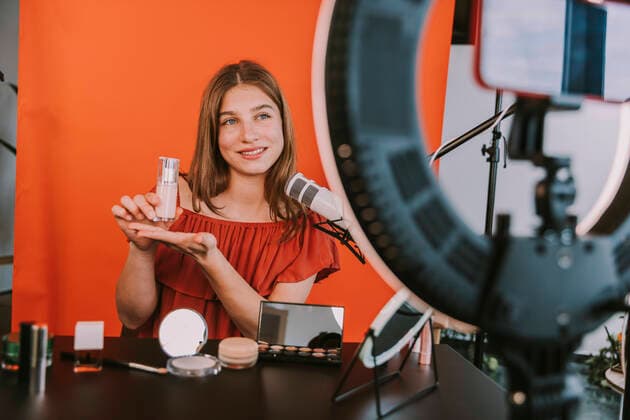 IMAGO Creative: Digitale Welt, Social Commerce Smiling female influencer presenting foundation while filming make-up tutorial at home workshop model released Symbolfoto property released MFF08190
