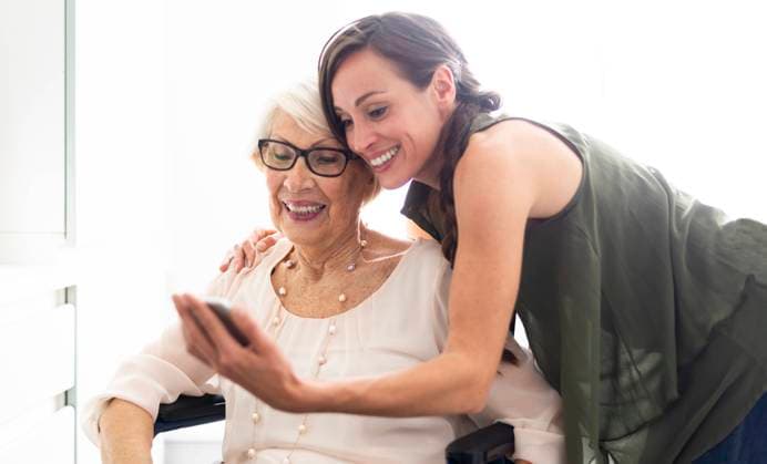 Smiling woman taking selfie with disabled grandmother through smart phone at home model released Symbolfoto property released OIPF00928