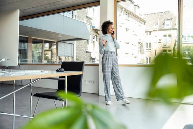 Smiling businesswoman gesturing while talking on mobile phone by window at office model released Symbolfoto property released UUF23265