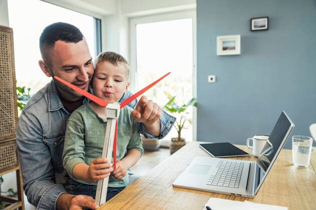 Smiling father sitting with son blowing wind turbine at home model released Symbolfoto property released UUF23379