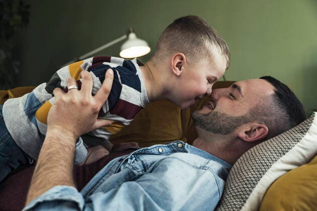 IMAGO Creative: Jahreszeit Winter, Couching Happy father embracing son while lying on sofa in living room at home model released Symbolfoto property released UUF23433