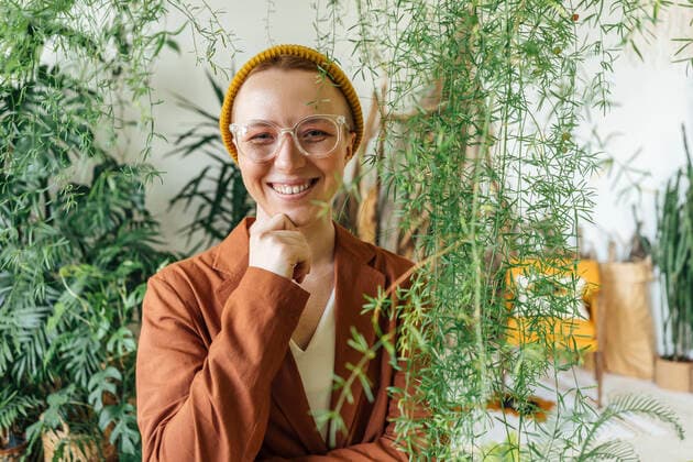 Smiling female entrepreneur with hand on chin standing by plants at work place model released Symbolfoto property released VPIF04136