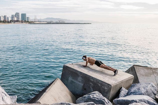 IMAGO Creative: Clickbait, Sport und Fitness Young male athlete doing push-ups on block shape rock by sea model released Symbolfoto XLGF01982