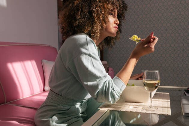 Creative Highlights Symbolbilder Side view of African American female eating salad while sitting at table with glass of wine and having tasty lunch at home, Model released, Property released Copyright: xJulioxRodriguezx MR