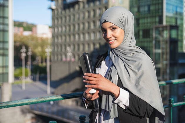 IMAGO Creative: Kreative Renaissance -- der junge Entrepreneur Cheerful Muslim female entrepreneur in hijab and with takeaway coffee standing in street looking at camera, Model released Copyright: xLuisxManuelxMunozx MR