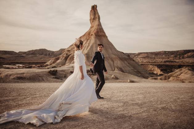 Creative Highlights Symbolbilder Happy groom and bride walking holding hands near mountain against cloudy sundown sky in Bardenas Reales Natural Park in Navarra, Spain, Model released Copyright: xOierxAsox MR