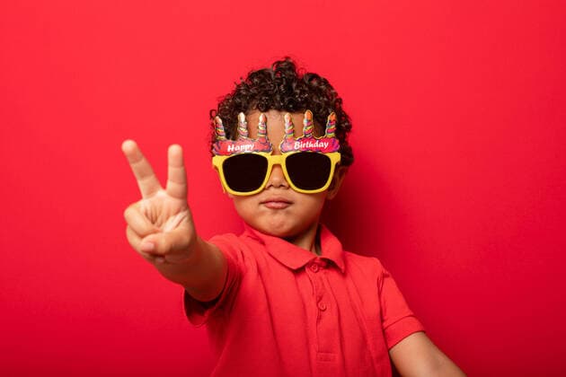 Geburtstag - Symbolbilder Creative Highlights Symbolbilder Cool child wearing bright Happy Birthday sunglasses showing peace gesture on red background in studio, Model released Copyright: xSheyxNunezx MR
