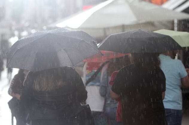 Personen gehen mit Regenschirmen während eines Regenschauers in der Innenstadt von Heidelberg, Baden Württemberg, Deutschland