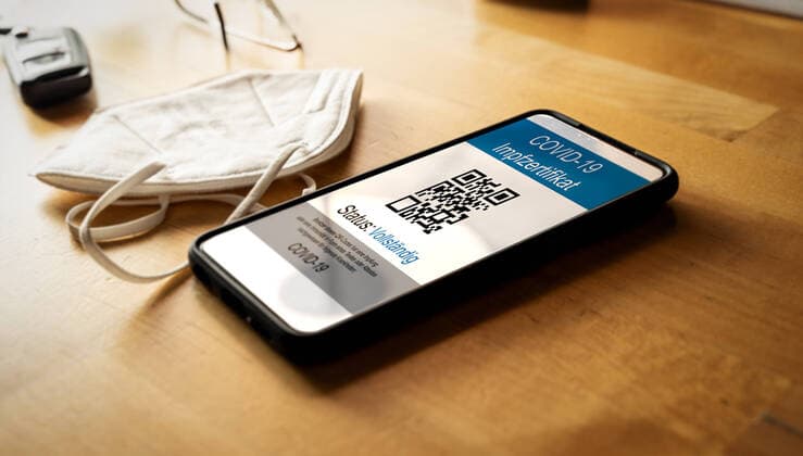 08 july 2021: A smart phone lying on a wooden table with a vaccinated digital health passport and a medical face mask.covid-19 european german vaccination certificate - impfpass