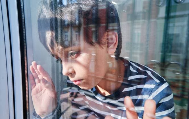 Through glass of unhappy preteen boy with bruises on face looking away while standing near window at home as concept of domestic violence and child abuse, Model released AdalbertoRodriguez_ChildAbuse_17.jpg Copyright: xAdalbertoxRodriguezx MR