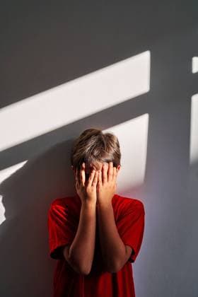 Upset unrecognizable boy covering face with hands and crying while standing near wall at home, Model released AdalbertoRodriguez_ChildAbuse_36.jpg Copyright: xAdalbertoxRodriguezx MR