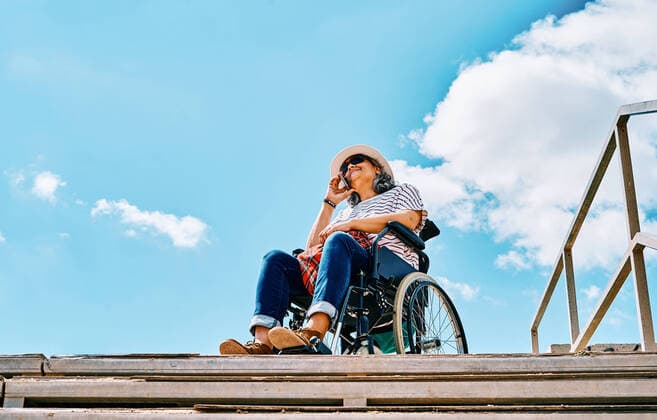 IMAGO Creative: NGO, Rehabilitation und Gesundheitswesen Mature disabled female sitting in wheelchair and talking on mobile phone near stairway against blue sky in city, Model released AdalbertoRodriguez_WomanInWheelchairBeach_24.jpg Copyright: xAdalbertoxRodriguezx MR