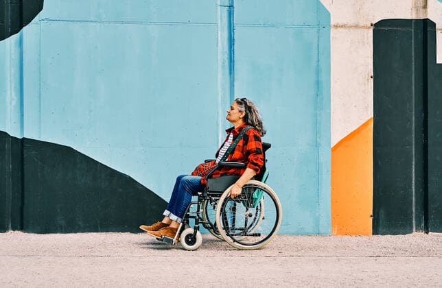 IMAGO Creative, Urban Lifestyle Full body side view of independent handicapped mature female riding wheelchair near painted wall on street, Model released AdalbertoRodriguez_WomanInWheelchairBeach_32.jpg Copyright: xAdalbertoxRodriguezx MR