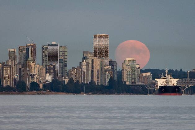 July 22, 2021, Vancouver, BC, Canada: A nearly full moon rises behind condo towers in the downtown skyline as a bulk carrier cargo ship sits at anchor on English Bay, in Vancouver, on Thursday, July 22, 2021. Vancouver Canada  - ZUMAc35_ 20210722_zaf_c35_044 Copyright: xDarrylxDyckx